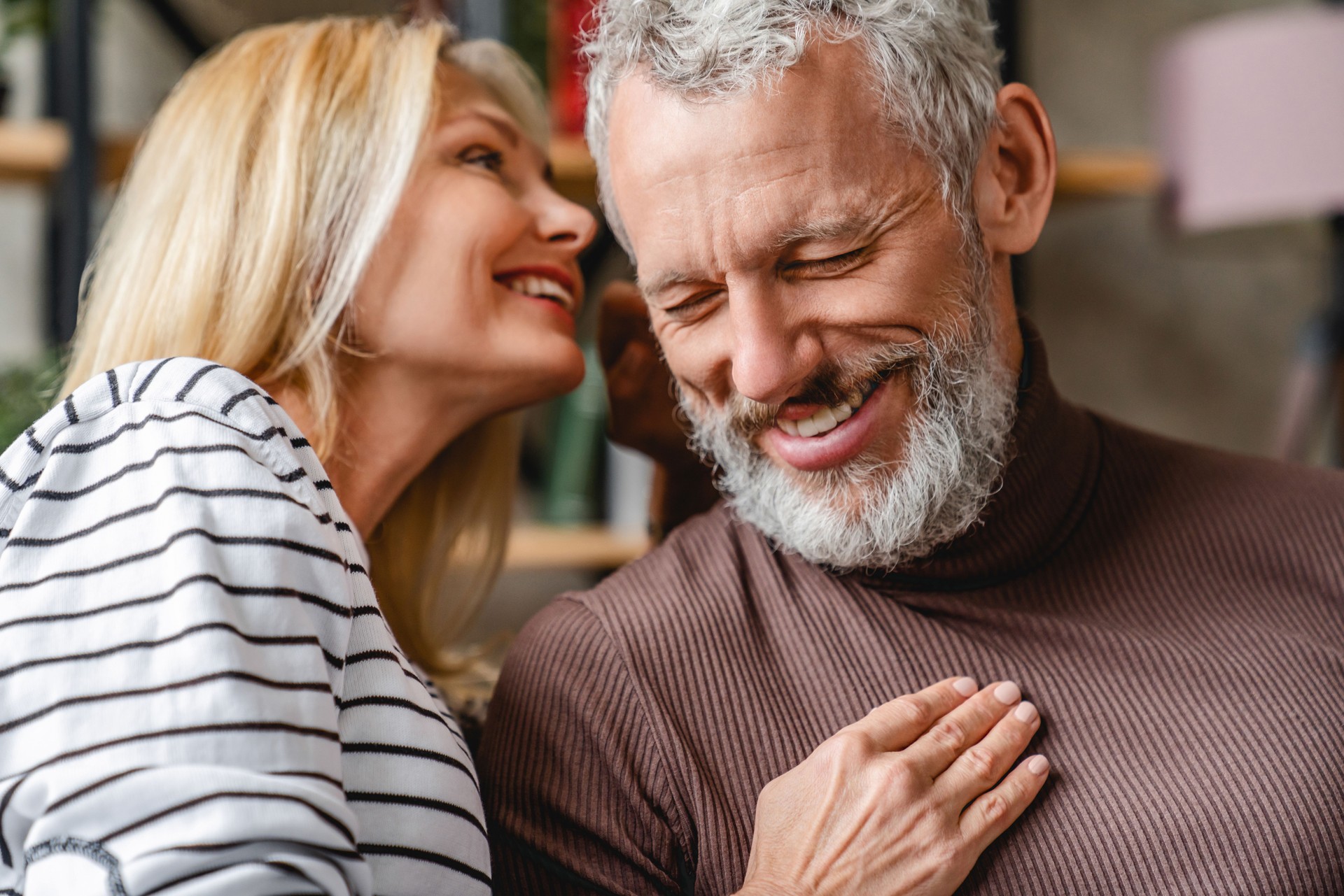 Senior man smiling while his beautiful loving wife whispering to his ear